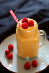 Mango and banana smoothie decorated with raspberries and reusable straw. Selective focus.