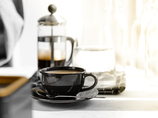 Coffee in black Cup on white background, table. French press,carafe of water, napkin, sunlight. Breakfast.