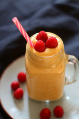 Mango and banana smoothie decorated with raspberries and reusable straw. Selective focus.