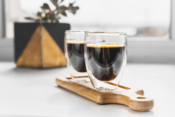 Two cups of fresh espresso on a wooden tray, on a white background. Sunlight from the window and...