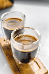 Two cups of fresh espresso on a wooden tray, on a white background. Sunlight from the window