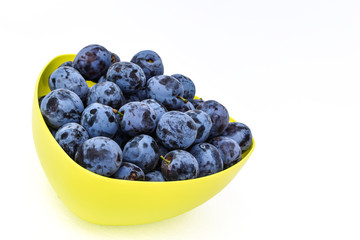 Fresh bright plums in the yellow bowl on white board