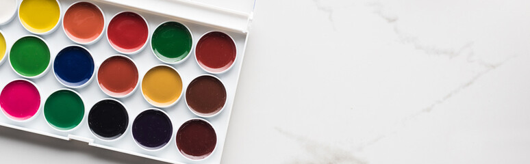 top view of watercolor paint palette on marble white surface with copy space, panoramic shot
