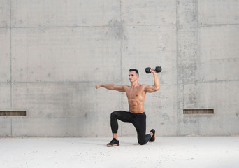 Muscular shirtless caucasian male athlete performs a dumbbell weightlifting exercise in a grungy...