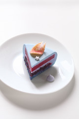 Contemporary Blue Matcha Mousse Cake with Black Currants covered with white chocolate velvet coating, on white background.