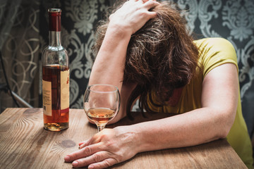 Drunk woman fell asleep at the table next to a bottle of liquor. Alcoholism concept