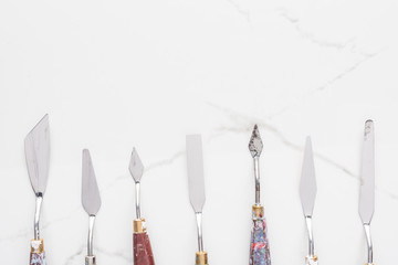 flat lay with metal spatulas for drawing on marble white surface with copy space