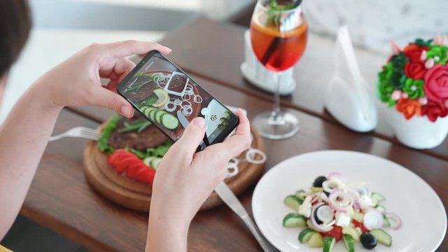 Food blogger hands using smartphone taking photo of beautiful beef steak on wood table inside the cafe to share on social media. Top view food photo. Lifistyle concept.