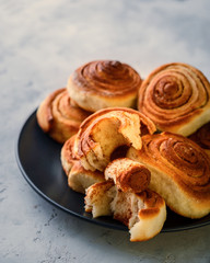 Handmade rolls with cinnamon on a dark dish and on a gray background.