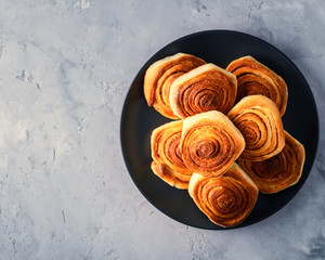 Handmade rolls with cinnamon on a dark dish and on a gray background.