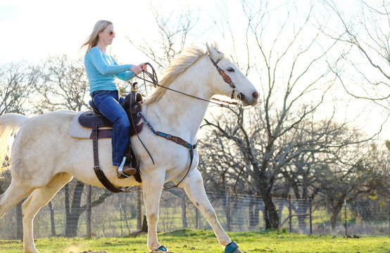 Horseback rider shows woman riding horse outdoors in pasture on farm.  Gray mare action, mane blowing for western lifestyle image.