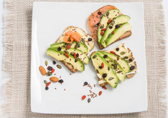 Salmon toast with avocado. Sandwich made with toast with slices of avocado and smoked salmon. Sesame seeds, walnut, linseed, goji berries.Top view.For healthy concept
