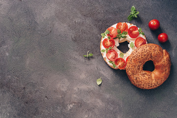Flat lay bagel sandwich with cream cheese, cherry tomatoes and basil sprinkled with sesame and flax...
