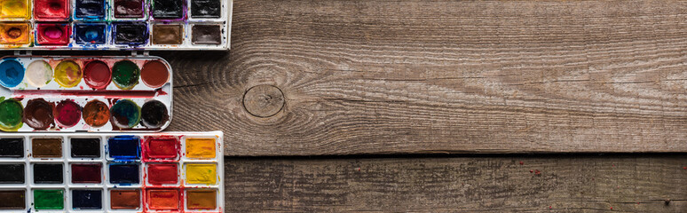 top view of colorful paint palettes on wooden brown surface with copy space, panoramic shot