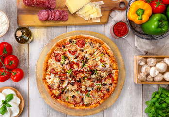 Fresh baked pepperoni pizza on wooden board and table, with colorful ingredients, overhead top view