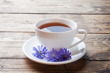Cup with chicory drink and blue chicory flowers on wooden table. Copy space.