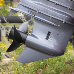 Gear of boat outboard motor, gray gearcase with black alloy 3 blade propeller on green grass background, lower unit maintenance © Ilya