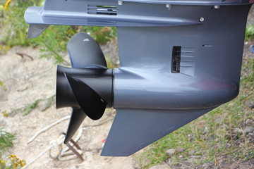 Black 3-blades boat prop on gear hub of new gray outboard boat motor, lower unit close up