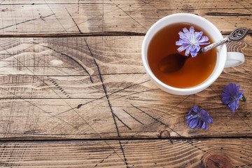 Cup with chicory drink and blue chicory flowers on wooden table. Copy space.