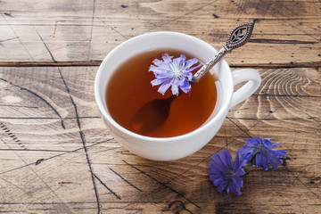 Cup with chicory drink and blue chicory flowers on wooden table. Copy space.