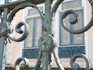 Detail of an old rusty iron fence. In the blurred background, windows of an old house. Clear and...