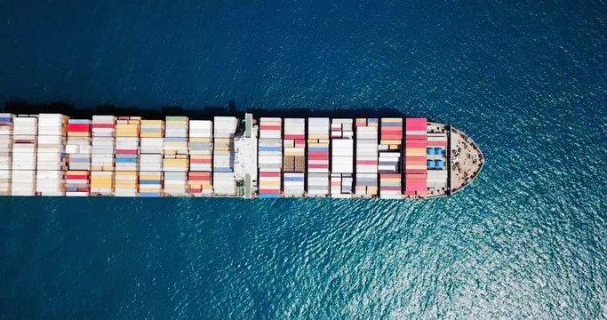 Aerial footage of a large container ship at sea, loaded with various container brands