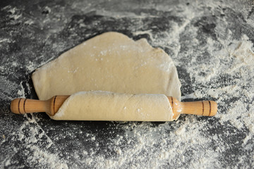 pizza dough is on the table, flour is scattered, rolling pin rolls out the cake