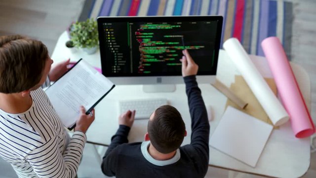 High angle view of two male programmers looking at code on computer screen, pointing with pencils on some details and discussing them