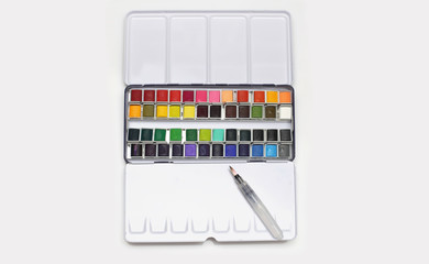 White metal box with watercolors, brush and palette on a light gray background.
