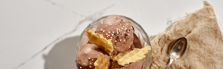 top view of delicious chocolate ice cream in bowl with waffles near brown cloth with spoon on marble grey background, panoramic shot