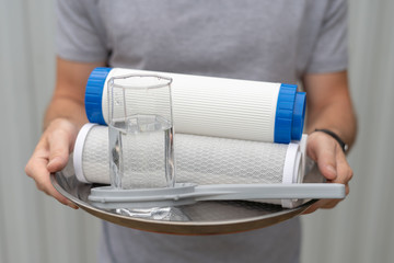 Man hold water filter with a glass of water and installation key on tray. Filtering cartridges...