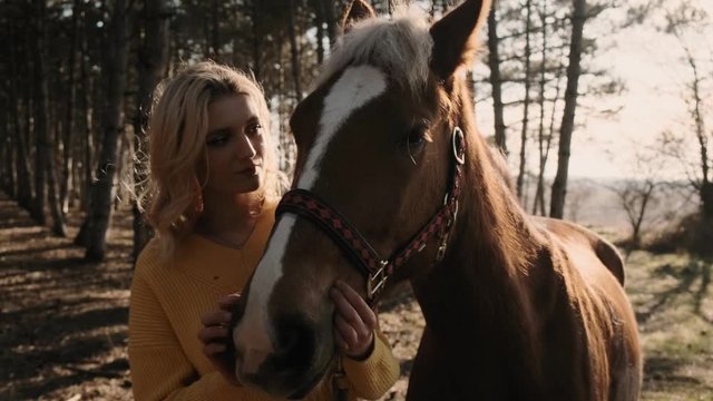 Beautiful blone woman is enjoing the hugging of sweet handsome horse in the wood close up slow motion
