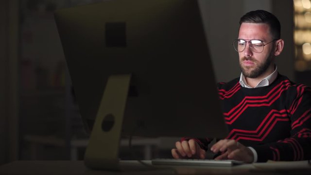 Tracking right of young stylish Caucasian man working at PC late in the evening