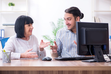 Young male employee explaining to old female colleague how to us