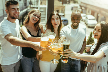 Young group of friends drinking beer, having fun, laughting and celebrating together. Women and men with beer's glasses in sunny day. Oktoberfest, friendship, togetherness, happiness, summer concept.