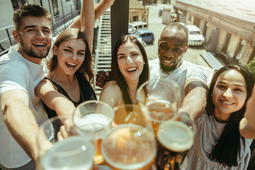 Young group of friends drinking beer, having fun, laughting and celebrating together. Women and men with beer's glasses in sunny day. Oktoberfest, friendship, togetherness, happiness, summer concept.