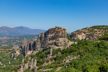 Meteora, Kalmbaka, Greece view overlooking world heritage Greek Orthodox monasteries in a green valley with village and mountains in the background. Breathtaking fairytale valley landscape.