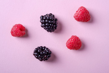 Raspberry and blackberry sweet organic juicy five berries on pink paper background, copy space