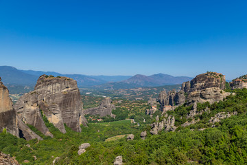 Fototapeta na wymiar Meteora, Kalmbaka, Greece view overlooking world heritage Greek Orthodox monasteries in a green valley with village and mountains in the background. Breathtaking fairytale valley landscape.