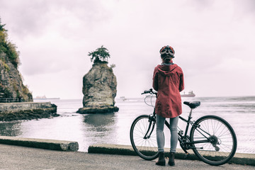Obraz premium Dziewczyna na rowerze na rowerze miejskim dojeżdża do pracy w Stanley Park, Vancouver, BC British Columbia, Kanada. Kobieta rowerzysta Vancouver na ścieżce rowerowej patrząc na Siwash rock.