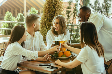 Young group of friends drinking beer, having fun, laughting and celebrating together. Women and men with beer's glasses in sunny day. Oktoberfest, friendship, togetherness, happiness, summer concept.