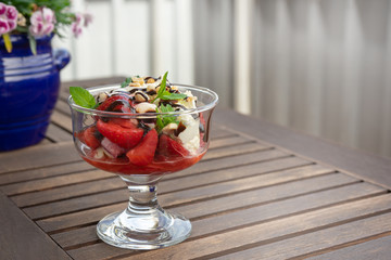 Ice cream with mint leaf and ripe berries in glass bowl, on light metallic and wooden background.