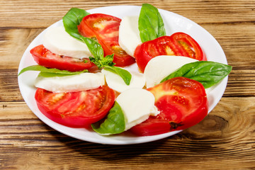 Italian caprese salad with tomatoes, mozzarella cheese and basil on a wooden table