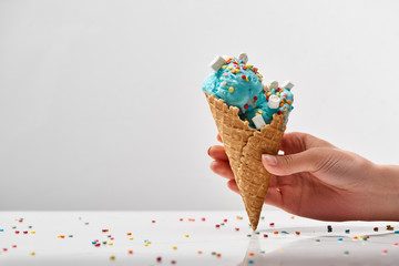 cropped view of woman holding delicious sweet blue ice cream with marshmallows and sprinkles in...