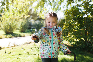 little white happy girl with two pigtails in a multi-colored jacket gathering pods from a tree on a warm autumn day