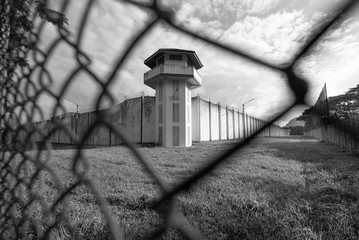 Prison watchtower protected by wire of prison fence.White prison wall and guard tower with coiled barbed wire.Criminal justice imprisonment concept - obrazy, fototapety, plakaty