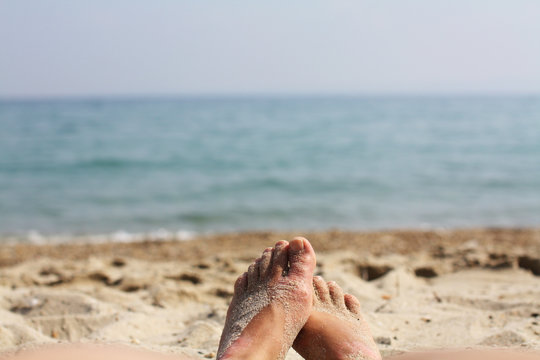 Female feet, sandy beach and sea in blur in the background. Picture with soft focus and place for your text. summer concept. Enjoying the sea or ocean. Focus is on feet. Vacation holidays. Copy space.