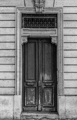 Black and white photo. Shabby door entrance of old building in Paris France. Antique wooden doorway and patterned metal grid on window of stone house. Classical style architecture in Europe.