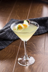 Green alcohol cocktail in martini glass with cucumber and yellow tomato on wooden table