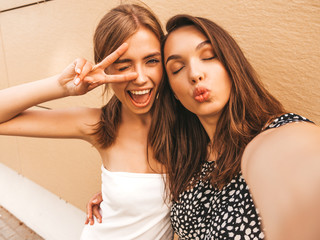Two young smiling hipster women in summer clothes. Girls taking selfie self portrait photos on...